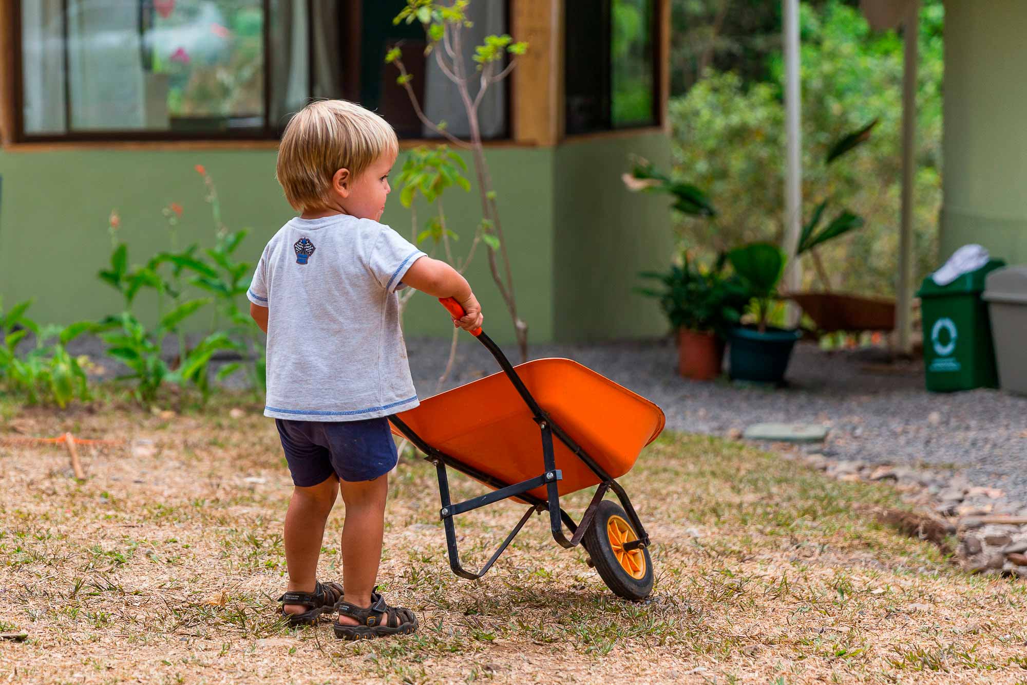 A small child pushing a wheelbarrow outside a home in the valley